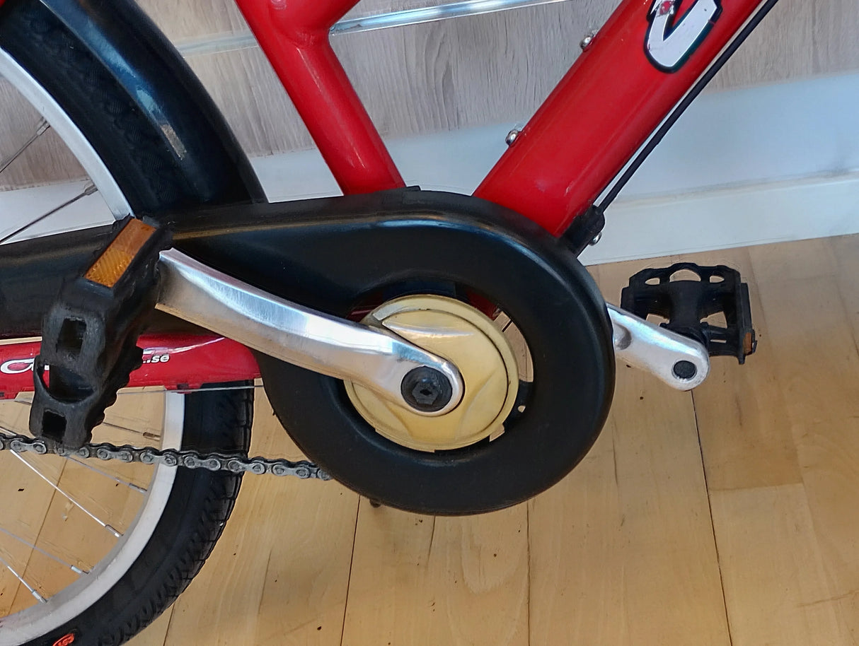 röd cykel vevarm, trampor, kedjeskydd, cykelkedja och hjul syns tydligt