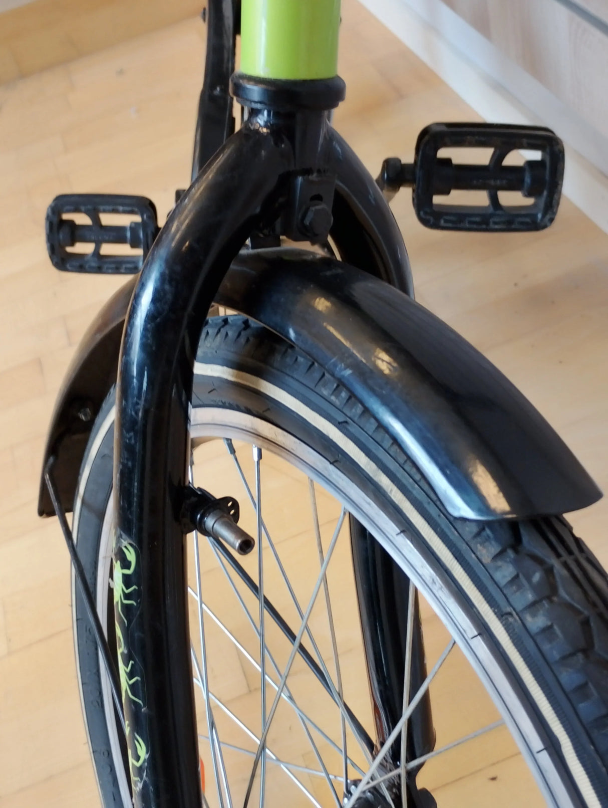 framgaffel och hjul på svart grön barncykel med reflex och pedaler, närbild