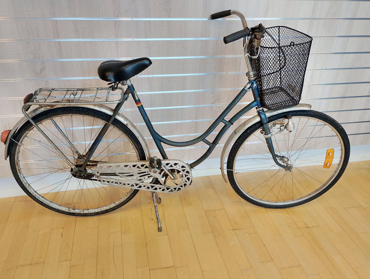 Gammal damcykel med korg, pakethållare och kedjeskydd på trägolv