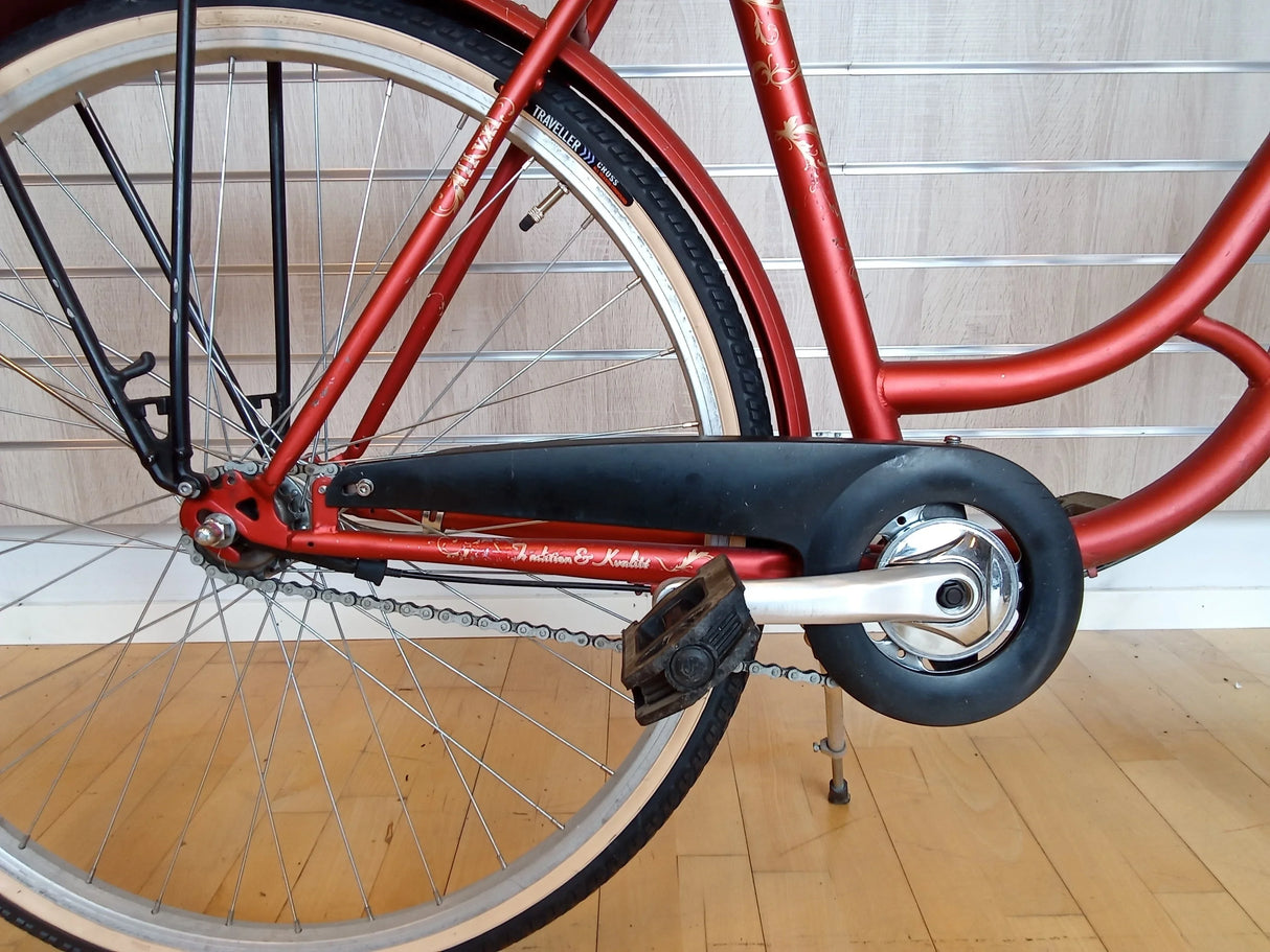 Rött cykelram och bakhjul med kedjeskydd och trampor på träunderlag