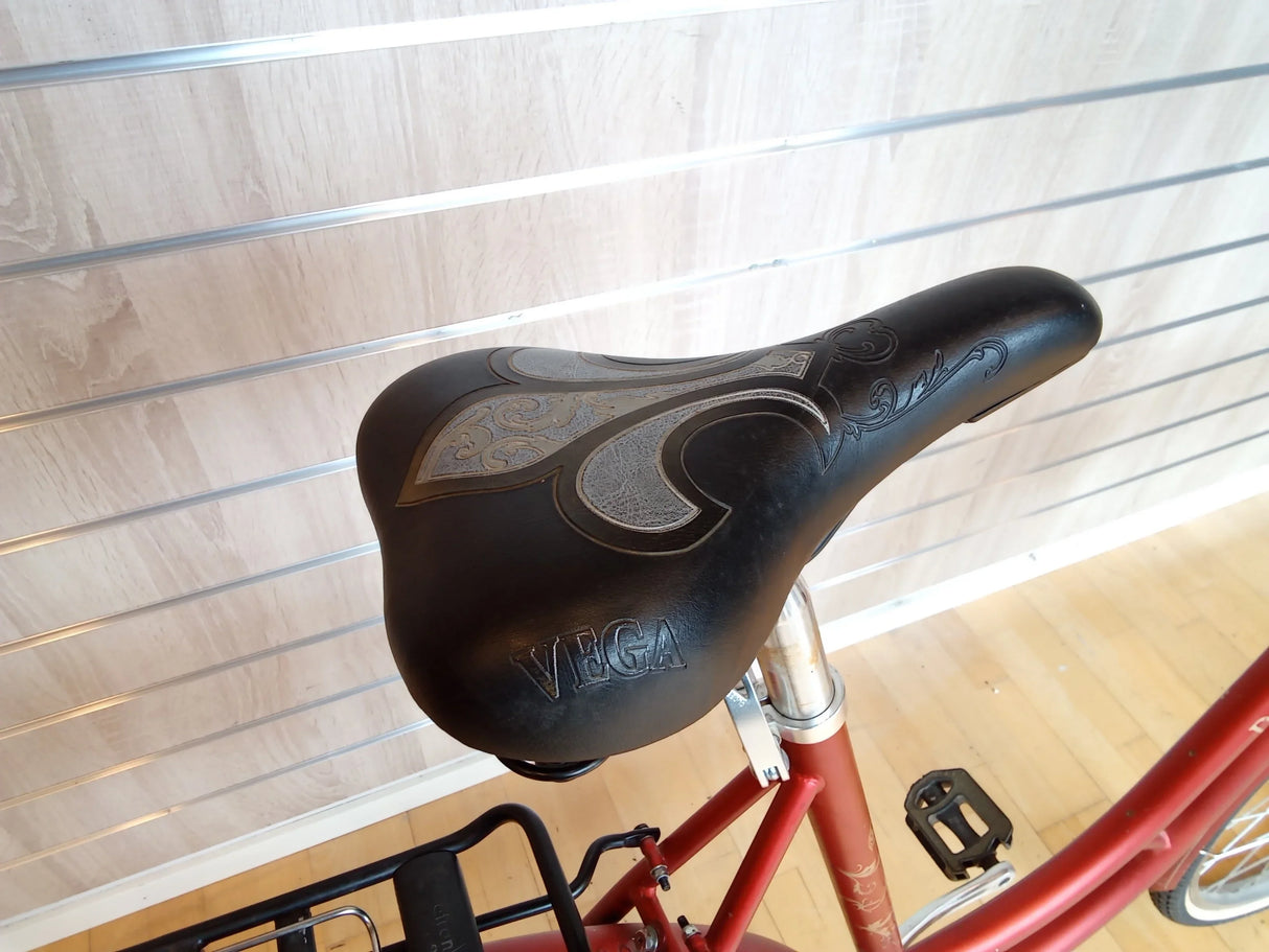 Svart cykelsadel med dekorativt mönster och texten VEGA på röd cykel