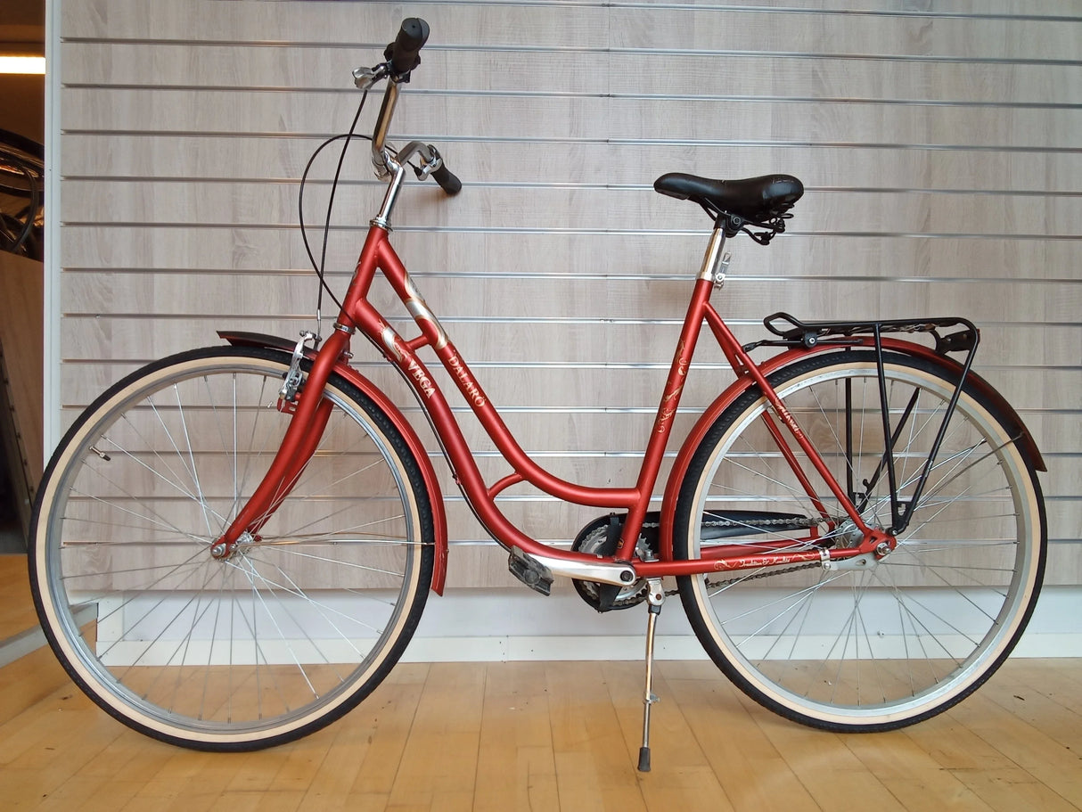 Röd damcykel med svart sadel, cykelställ och vita däck på trägolv