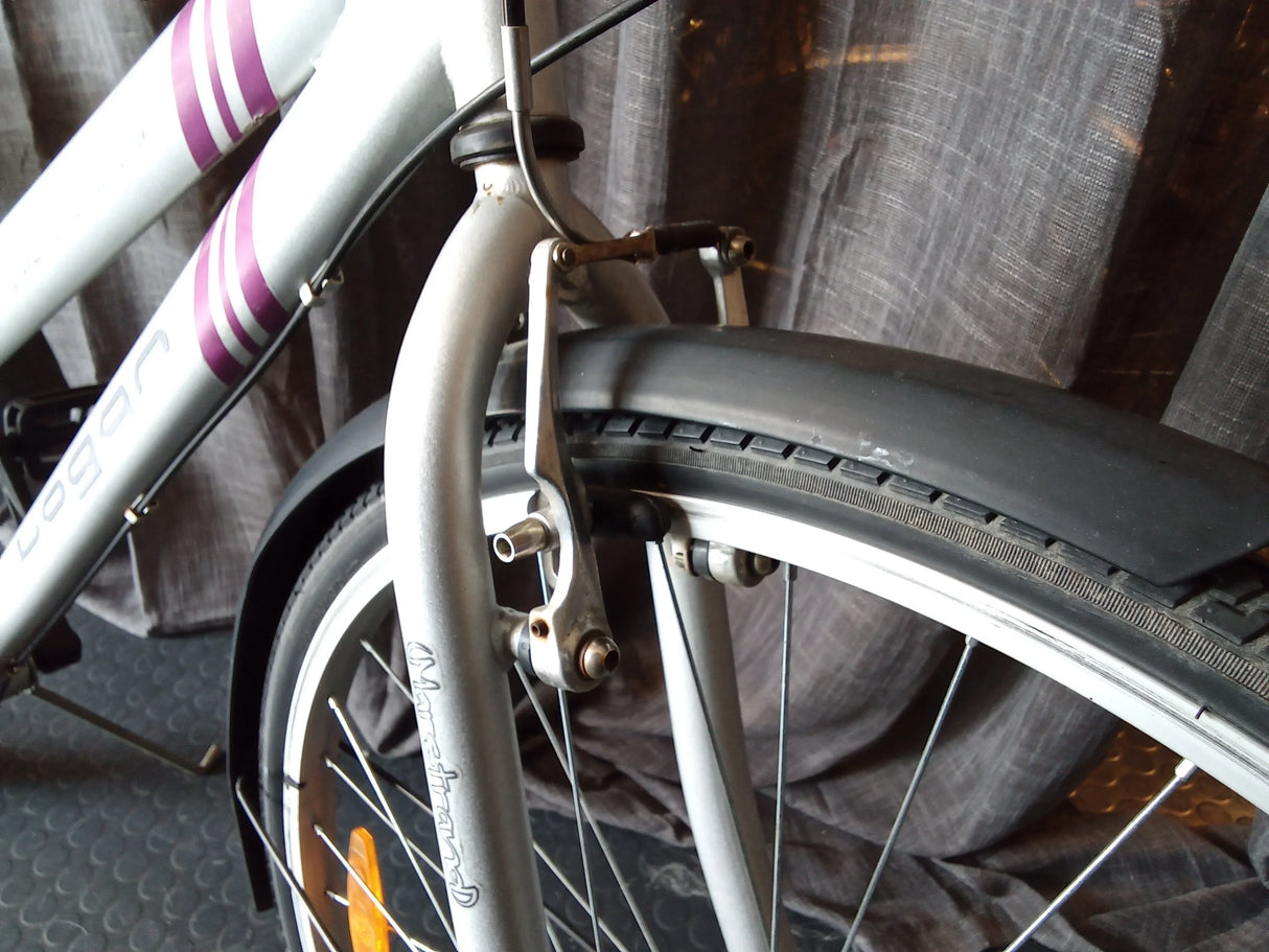 Närbild av framhjul och broms på silverfärgad cykel med svarta däck och lila ränder