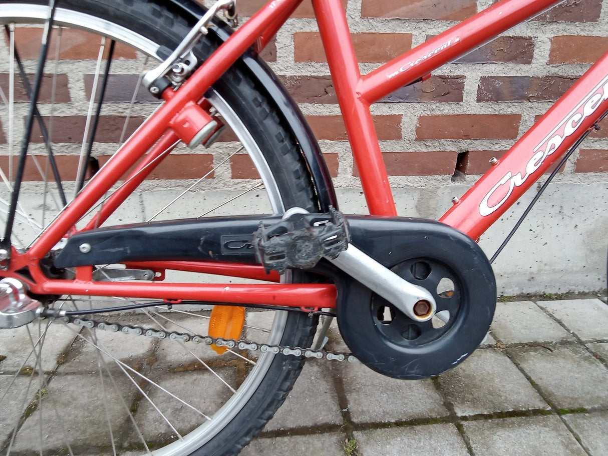 Röd Crescent cykel med svart kedjeskydd och pedal, närbild på kedja och bakhjul