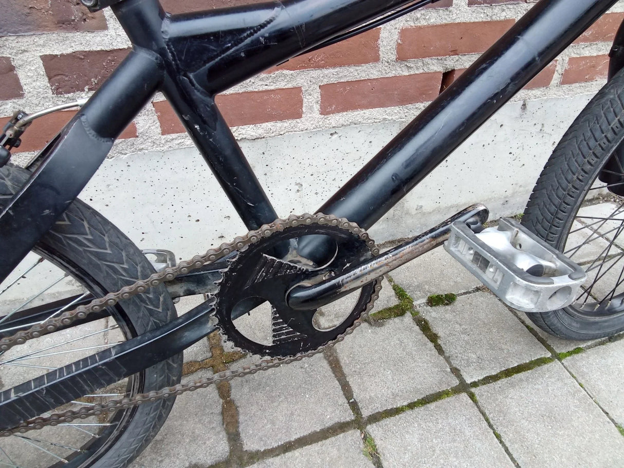Svart cykel med sliten kedja och pedal vid trottoar