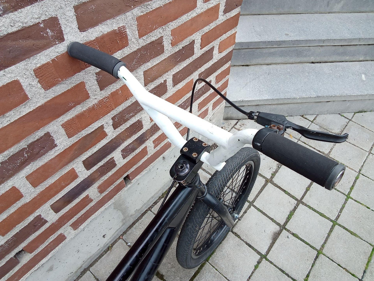 Närbild på cykelstyre med vita handtag och svart bromshandtag på framhjul
