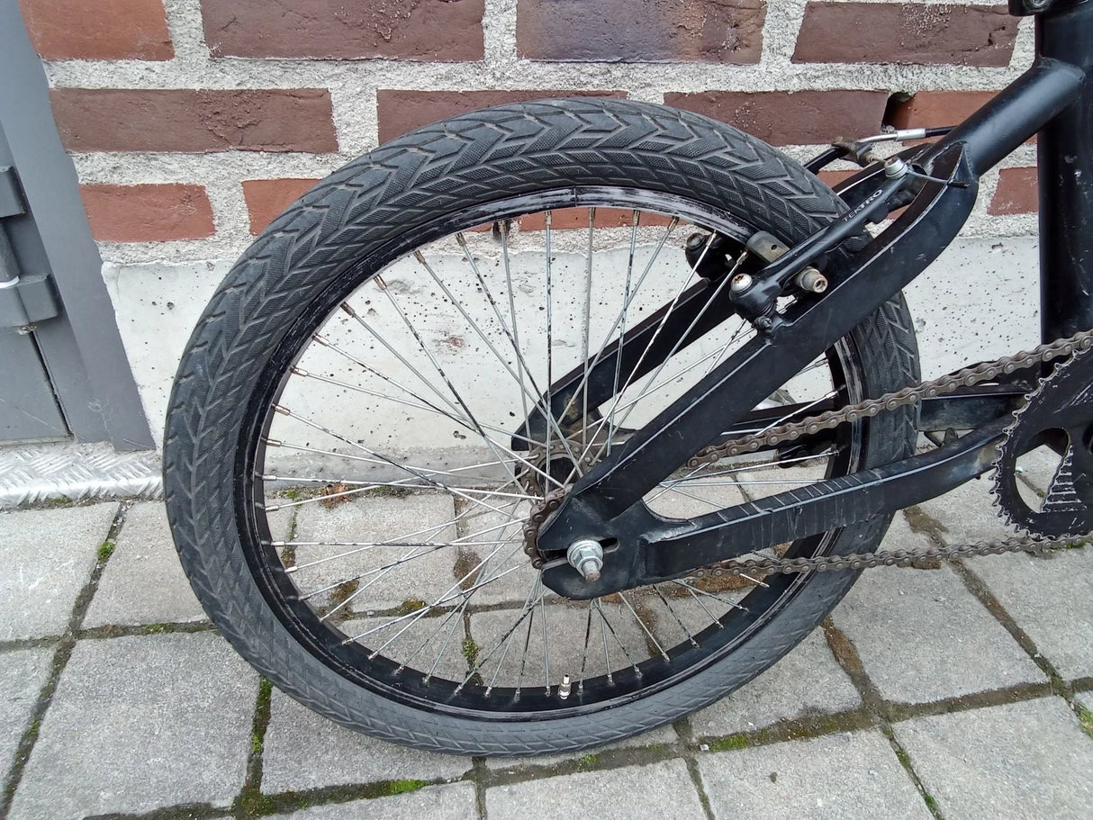 Svart BMX-cykelhjul med gummidäck och kedja mot tegelvägg och stenplattor