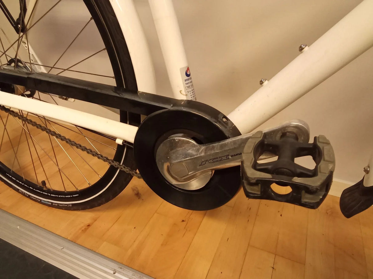 Närbild på vit cykel med svart kedjeskydd, silver vevarm och svart pedal