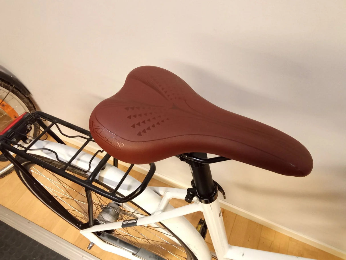 Brun cykelsadel på vit Nishiki cykel med svart pakethållare och bakhjul