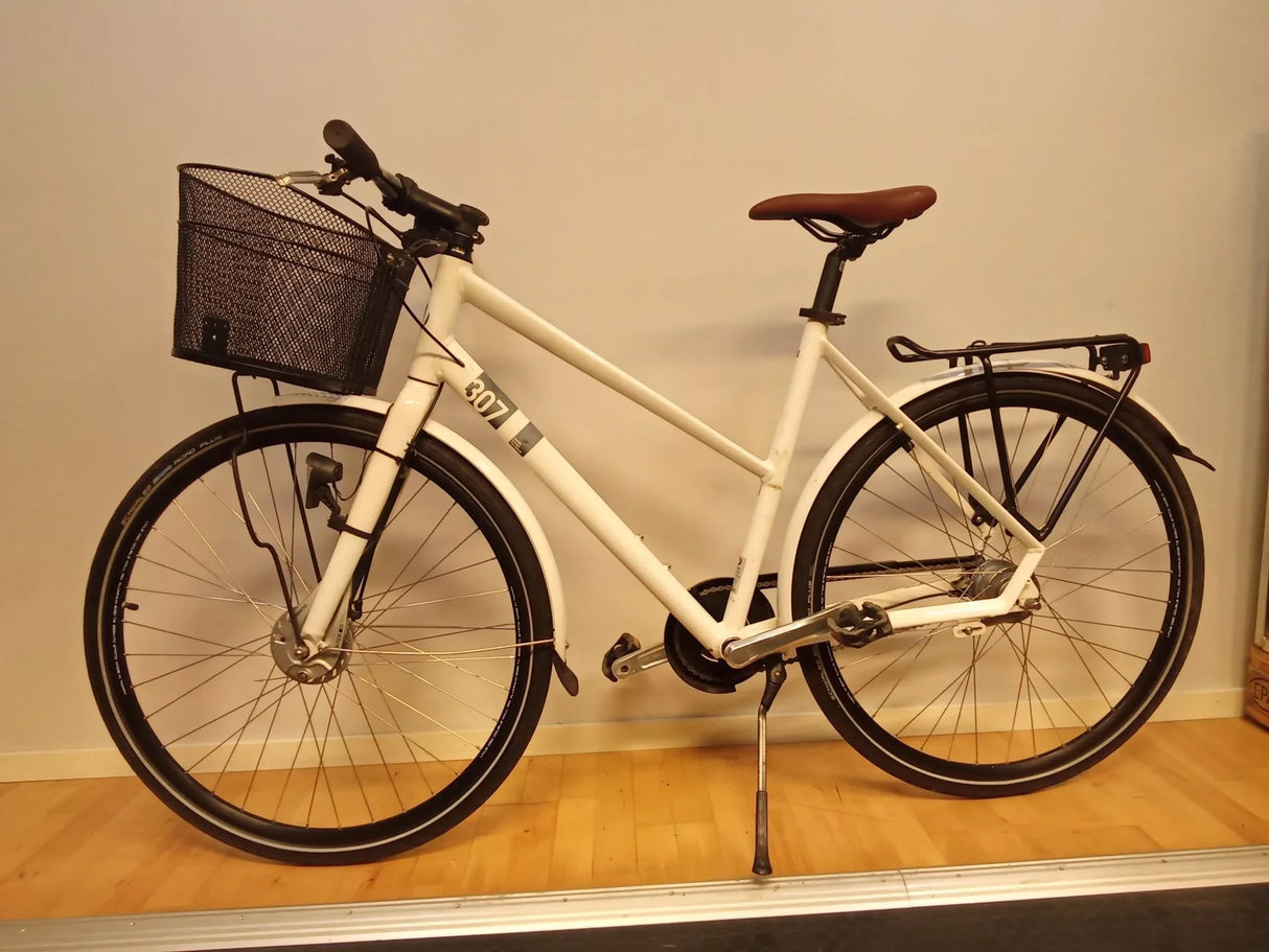 Vit stadscykel med svart korg fram, brun sadel och pakethållare