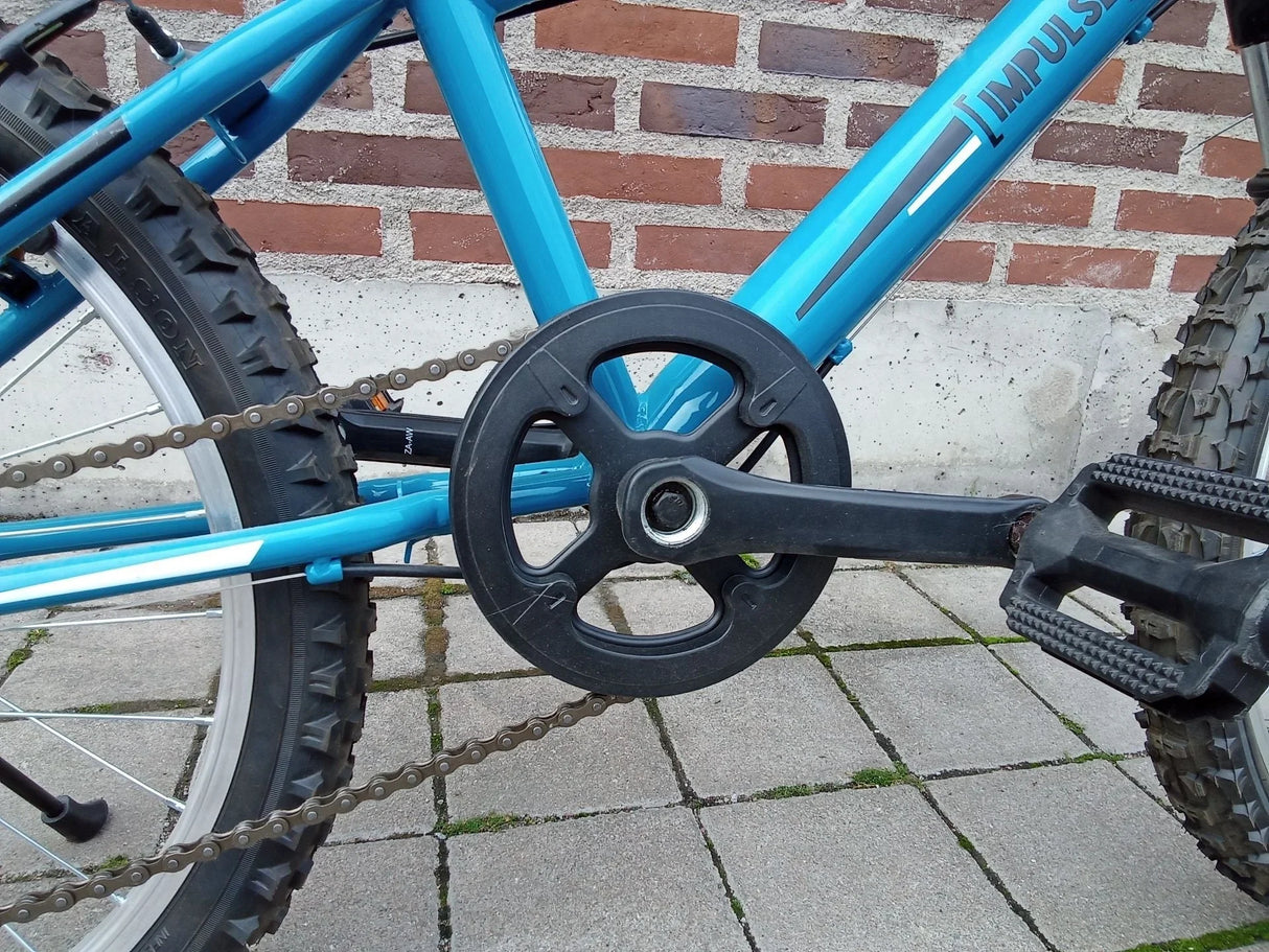 Närbild på blå Impuls cykelns kedjehjul, svart pedal och slitstark däckstruktur