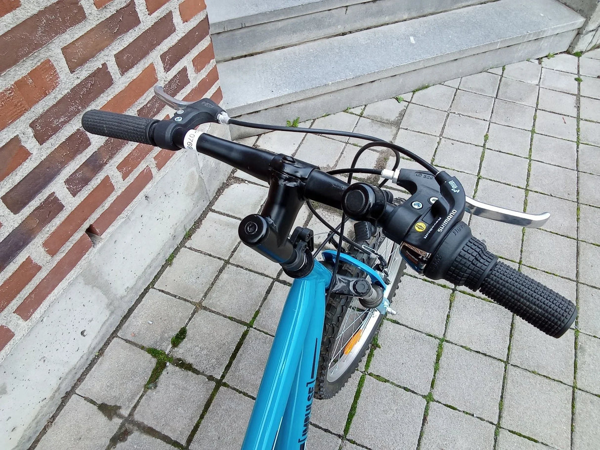 Blå mountainbike med svarta styrhandtag och Shimano växelreglage på asfalt