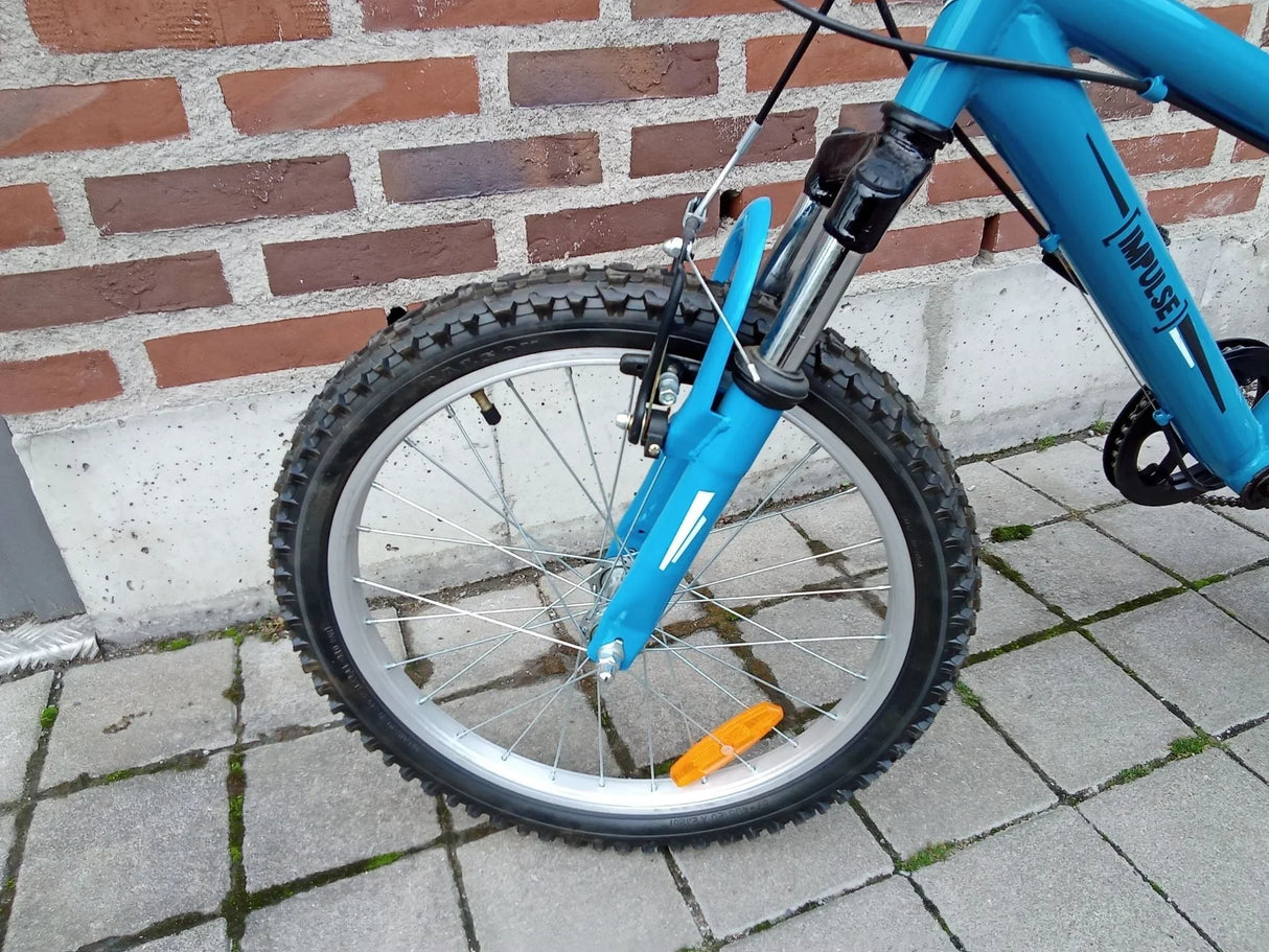 Framhjul på blå Impulse mountainbike med tjockt mönstrat däck och metalldetaljer