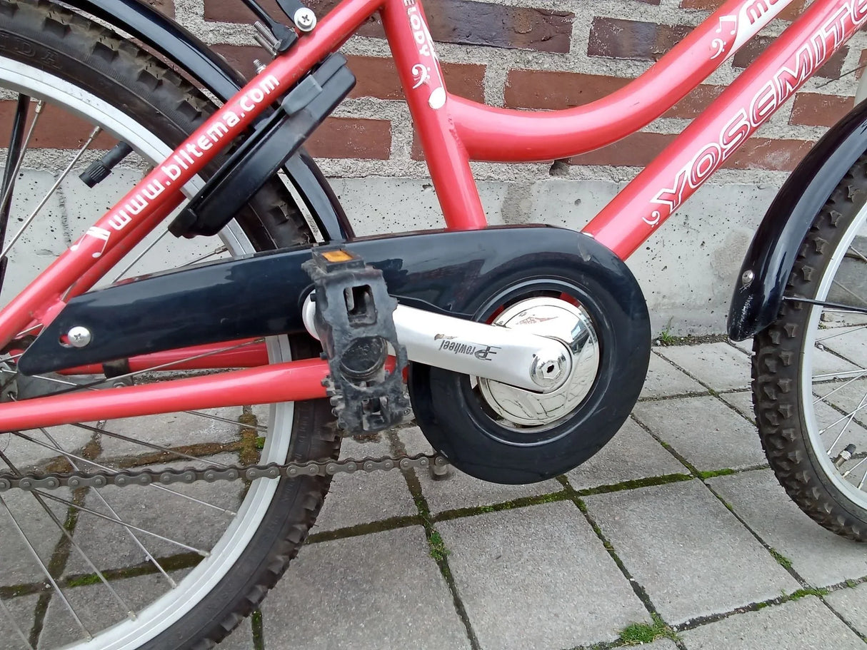Röd barncykel Yosemite med kedjeskydd och pedaler på gatsten