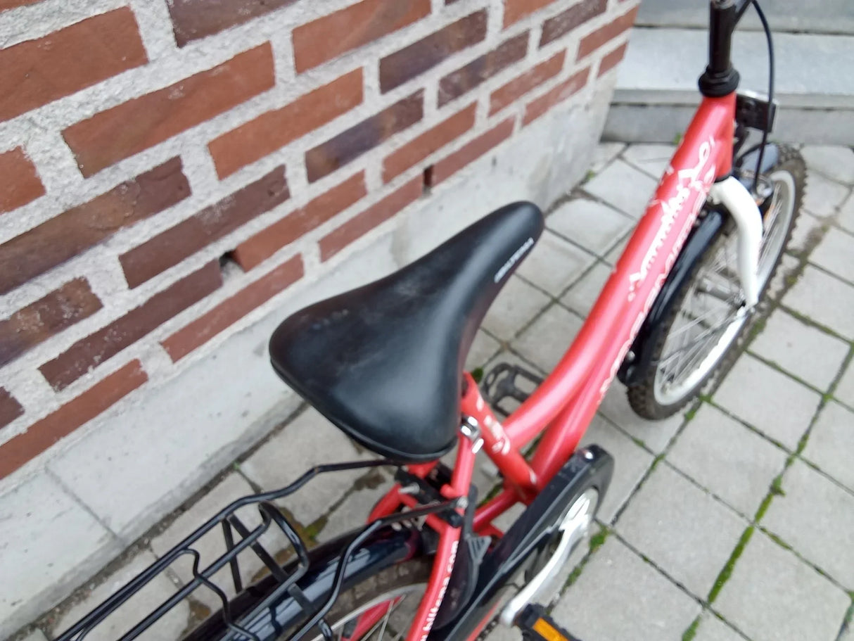 Röd barncykel med svart sadel och vita däck på stenläggning