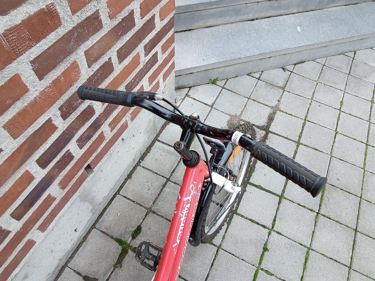 Röd och vit barncykel med svart styre och grepp på stenbelagd mark