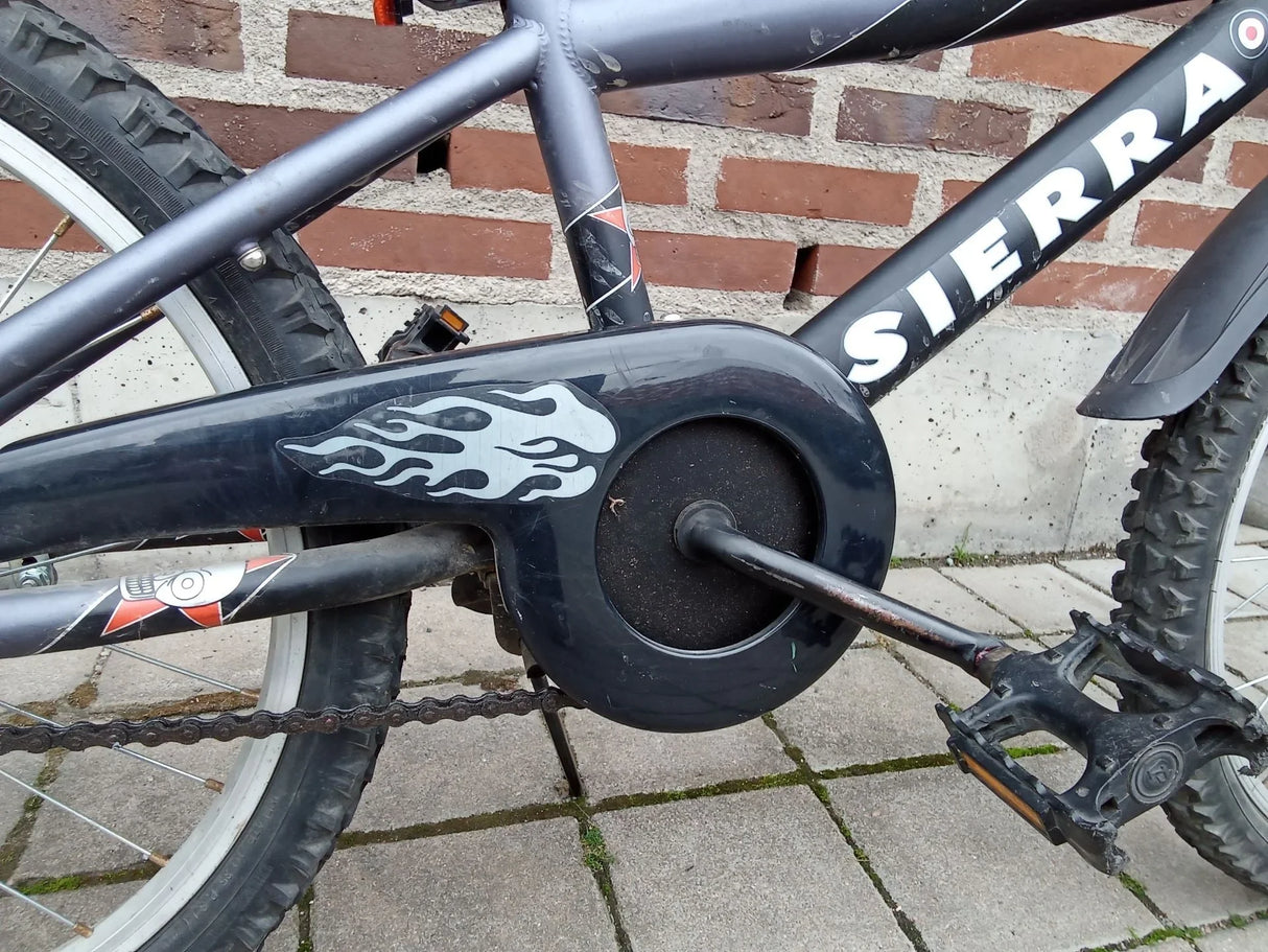 Svart cykelkedjeskydd med vit eldmönster och pedal på barncykel Sierra