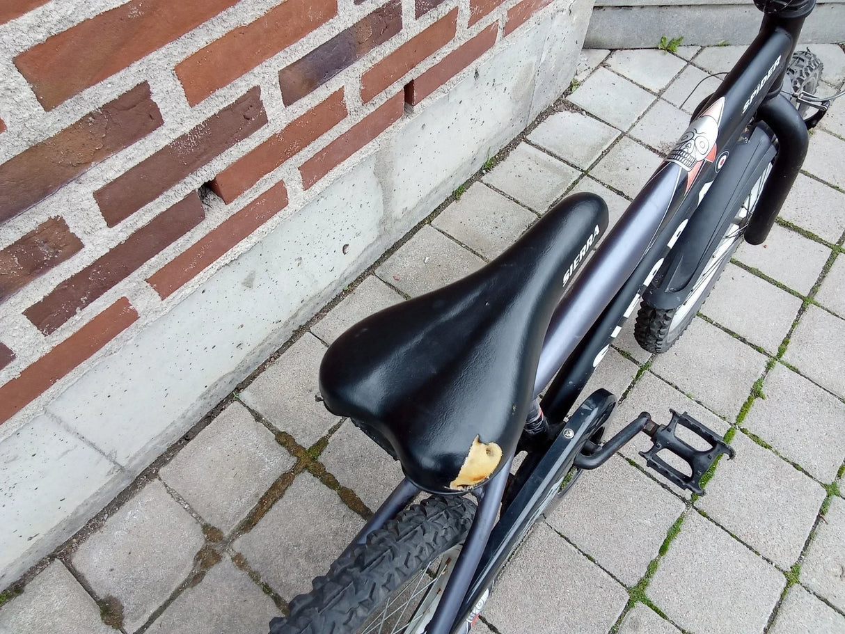 Svart cykelsadel Sierra med slitna partier på en mountainbike med grovmönstrade däck