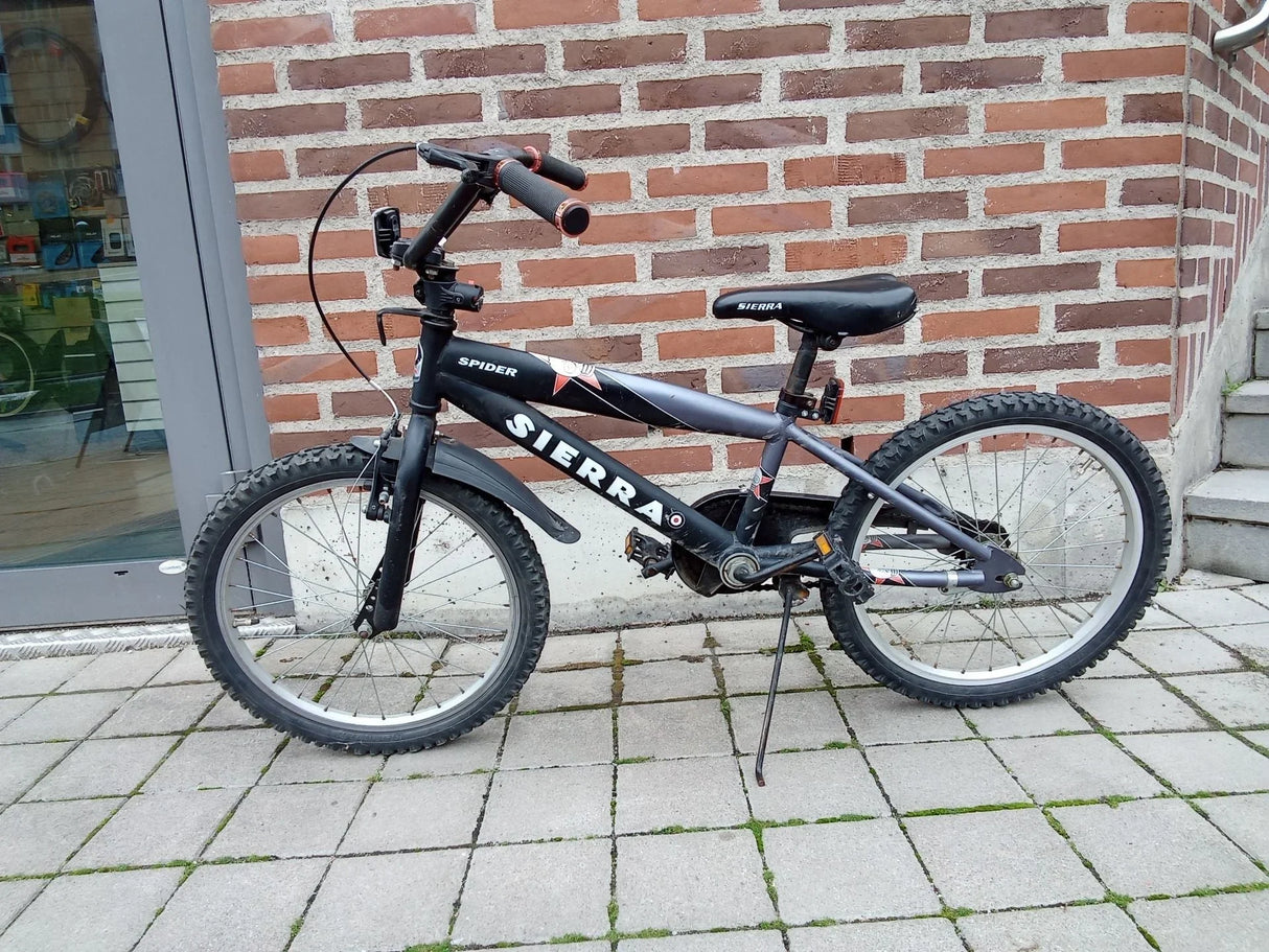 Svart barncykel Sierra Spider med tjocka däck och stänkskydd parkerad på stenläggning