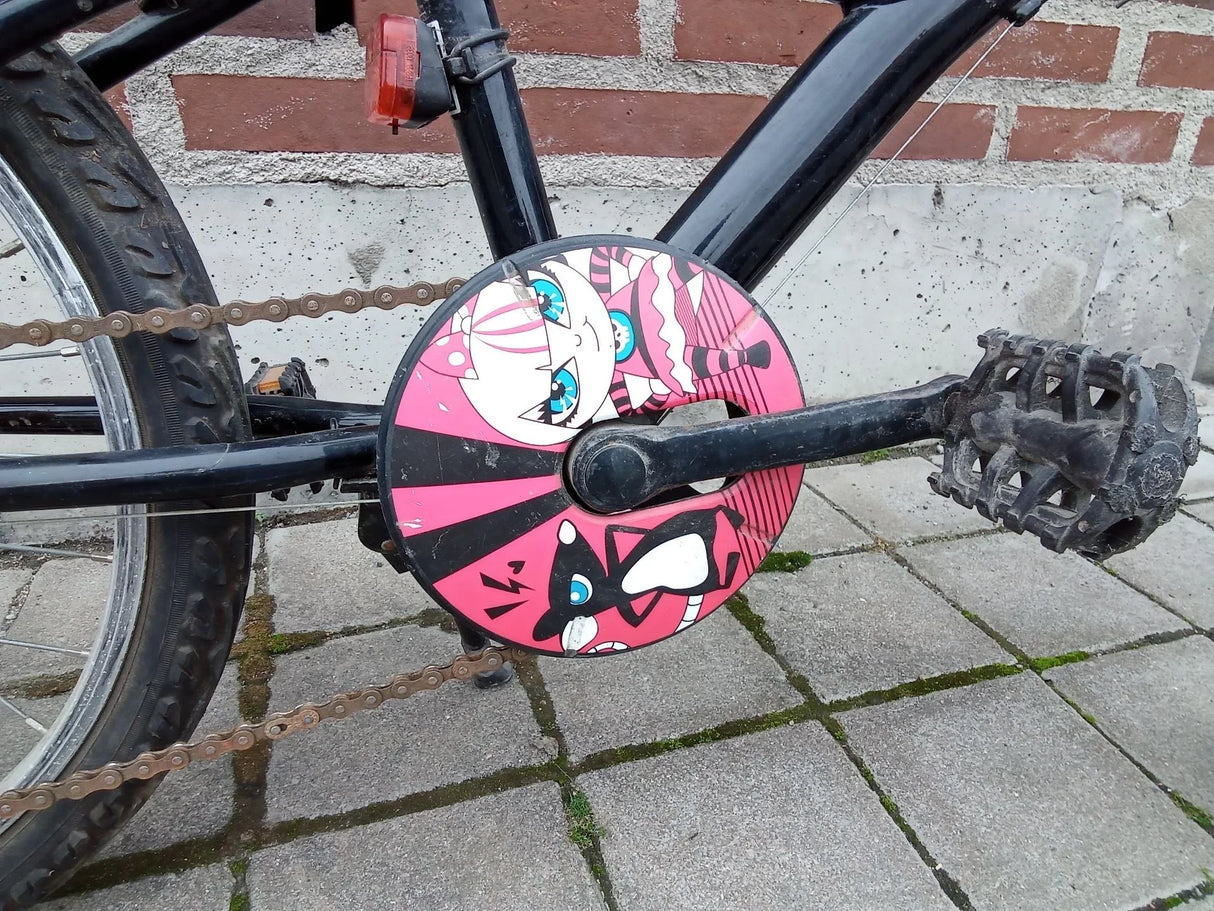 Cykelpedal och kedjeskydd med rosa och svart tecknad figur på svart cykel