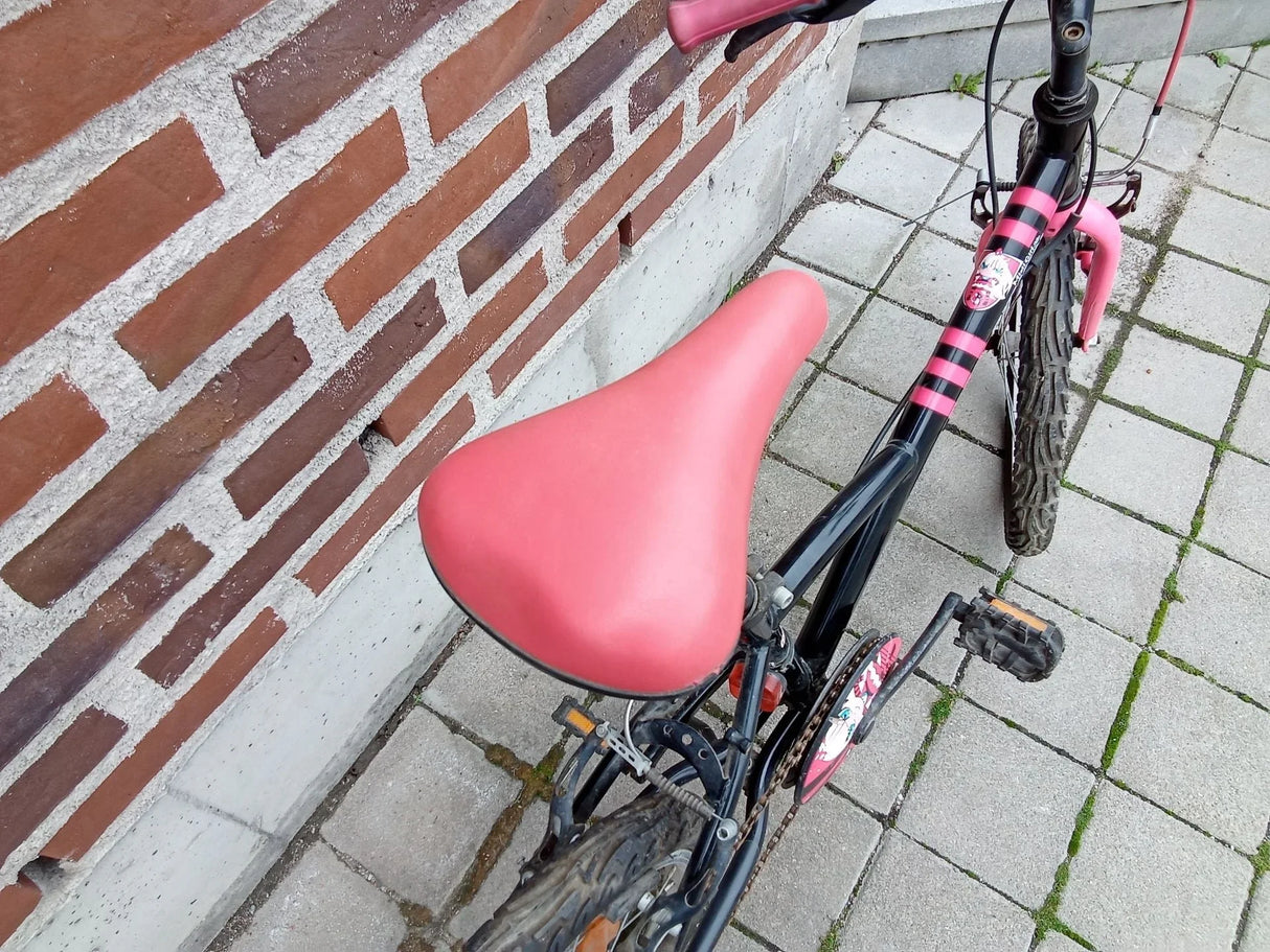 Svart och rosa barncykel med rosa sadel och rutor på stenbelagd mark