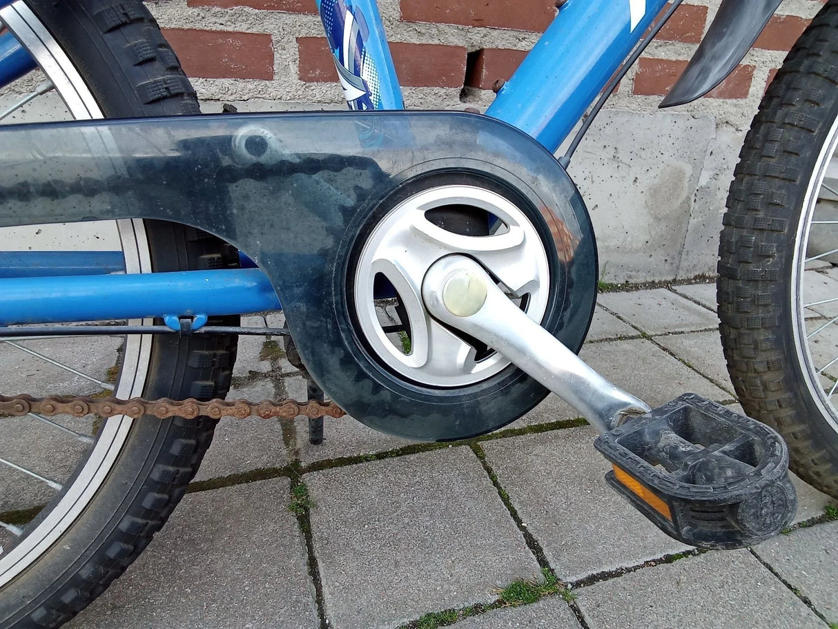 Blå cykelpedal och kedjeskydd med svart plast och metallkomponenter på trottoar