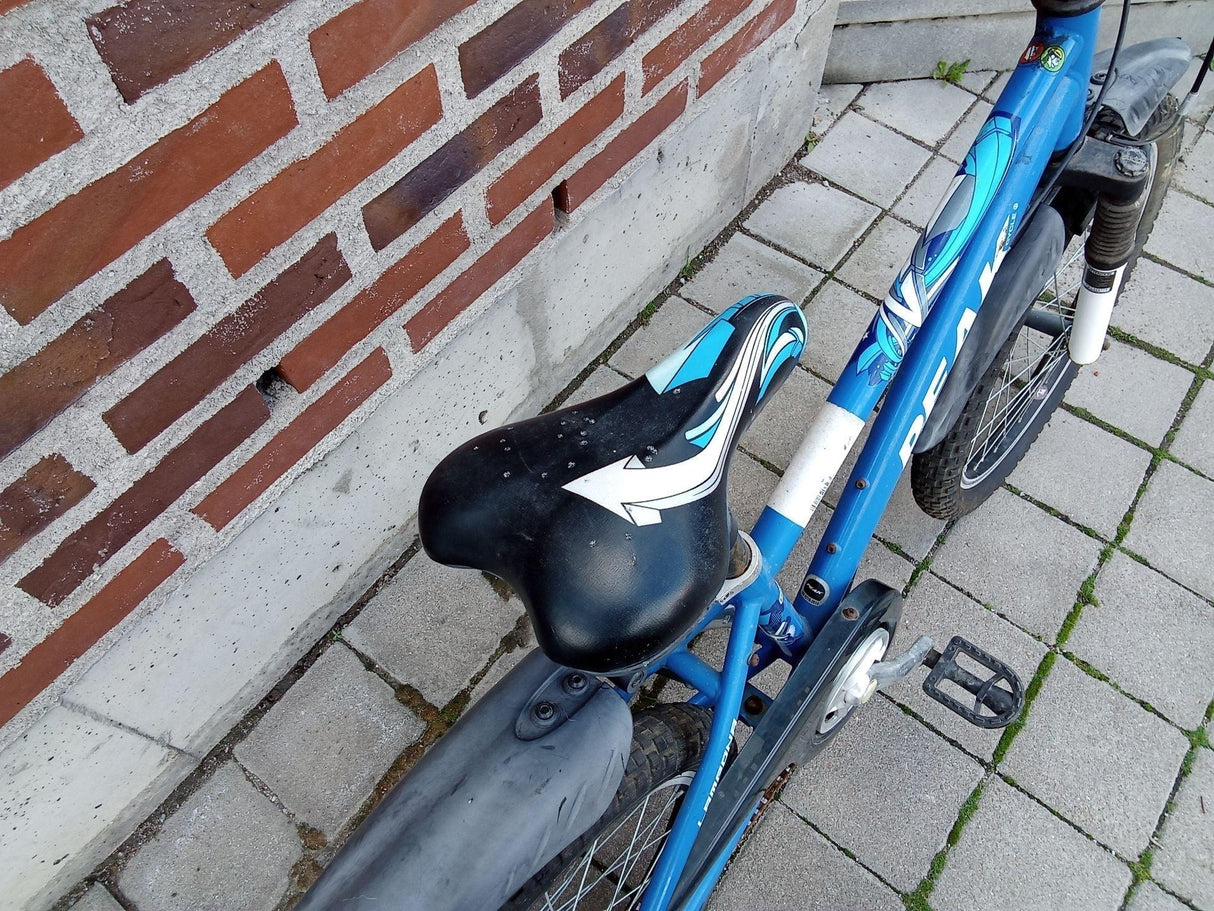 Blå barncykel med svart sadel och stadiga däck på stenlagd trottoar