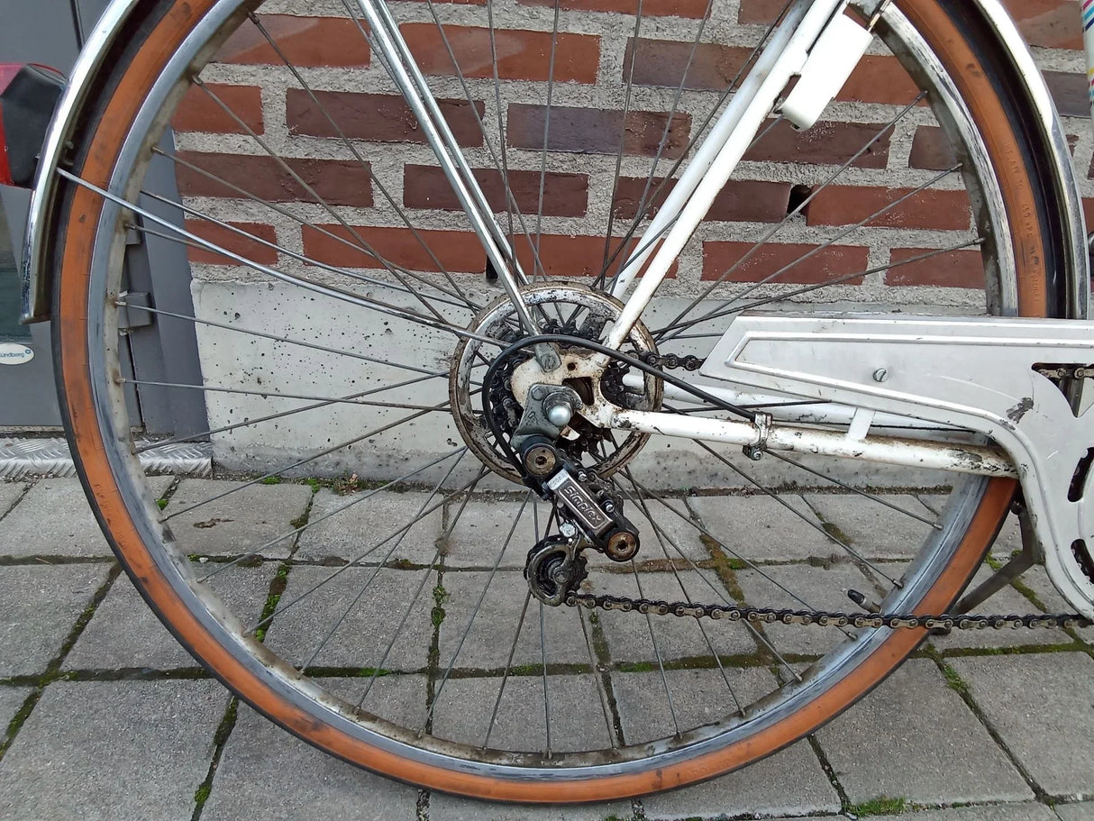 Närbild på cykelns bakhjul med kedja, växel och brun kantad däck