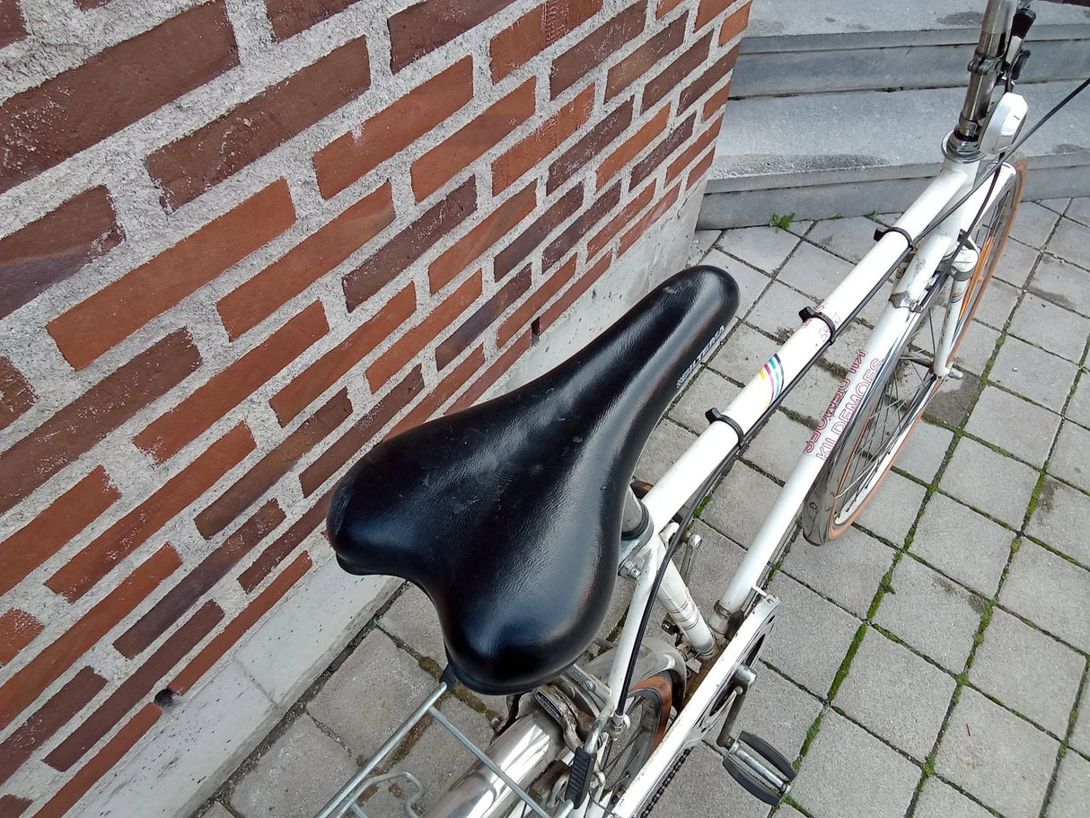 Vitt landsvägs- eller sportcykel med svart sadel och orange däck på stenlagd yta