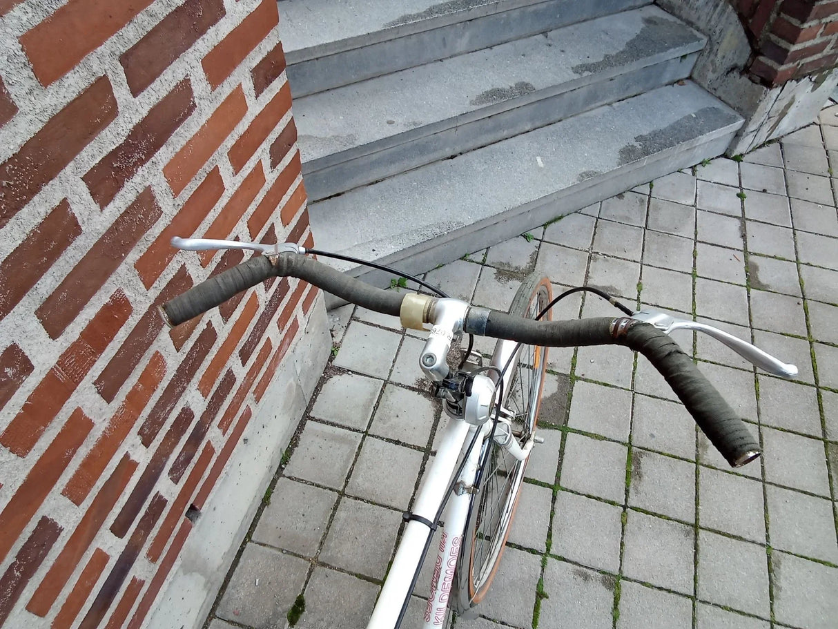 Vitt cykelstyre med svart ringat grepp och silver bromshandtag på stenplattor
