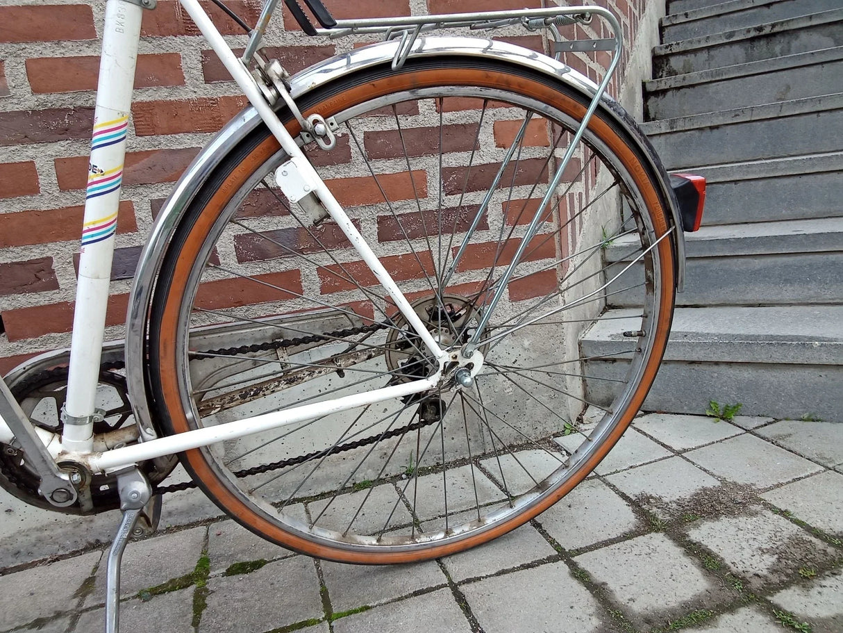 Närbild på cykelns bakhjul med orange däck och kedjehus i vitt