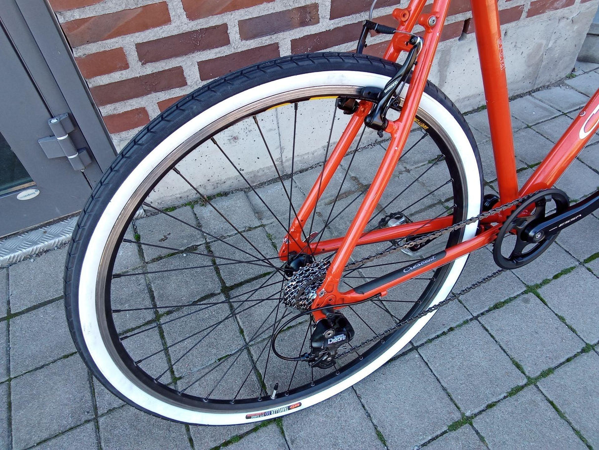 Närbild på orange cykel med vita däck, Shimano Deore växel och svart kedja