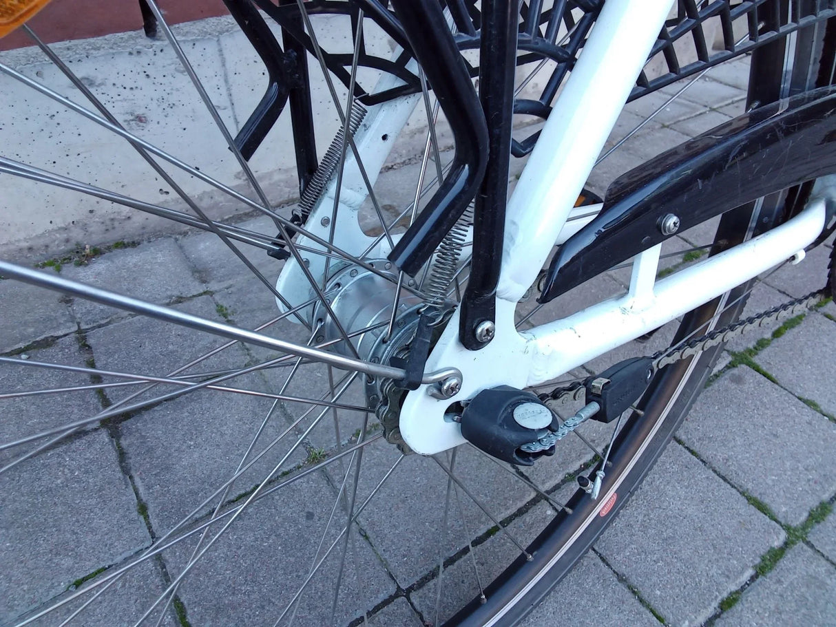 Närbild på bakhjul med ekrar, kedja och kedjespännare på vit cykelram