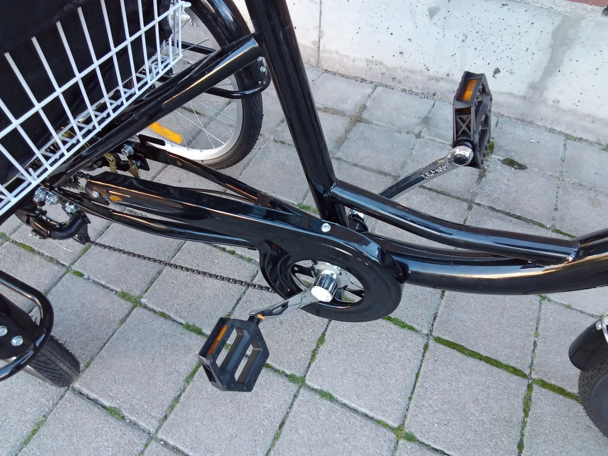 Detalj av svart trehjulig cykel med pedaler, kedja och vit lastkorg