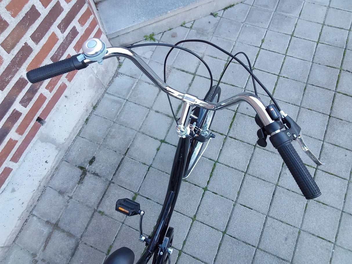 Svart cykel med kromade styre och ringklocka på stenlagd mark
