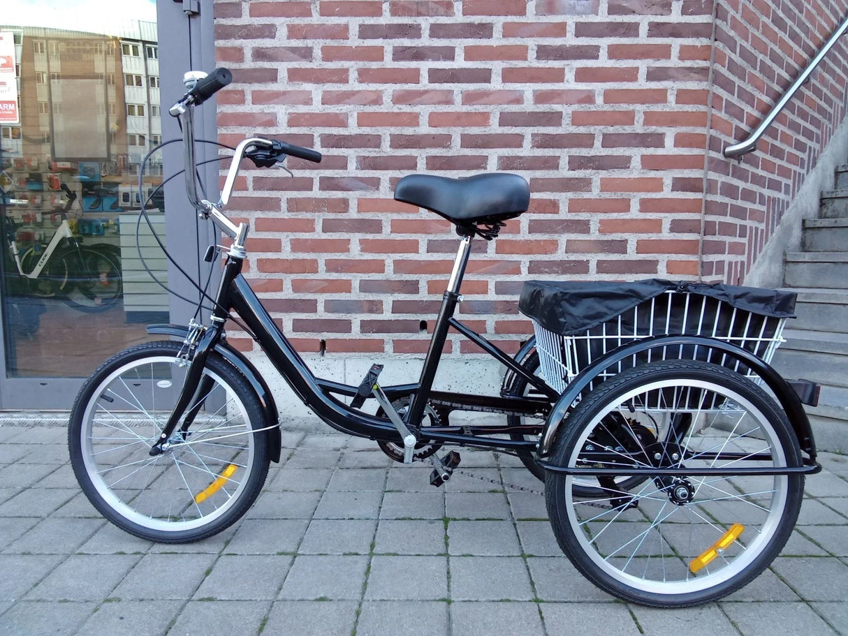 Svart trehjulig lastcykel med korg och sadel på stenbelagd yta