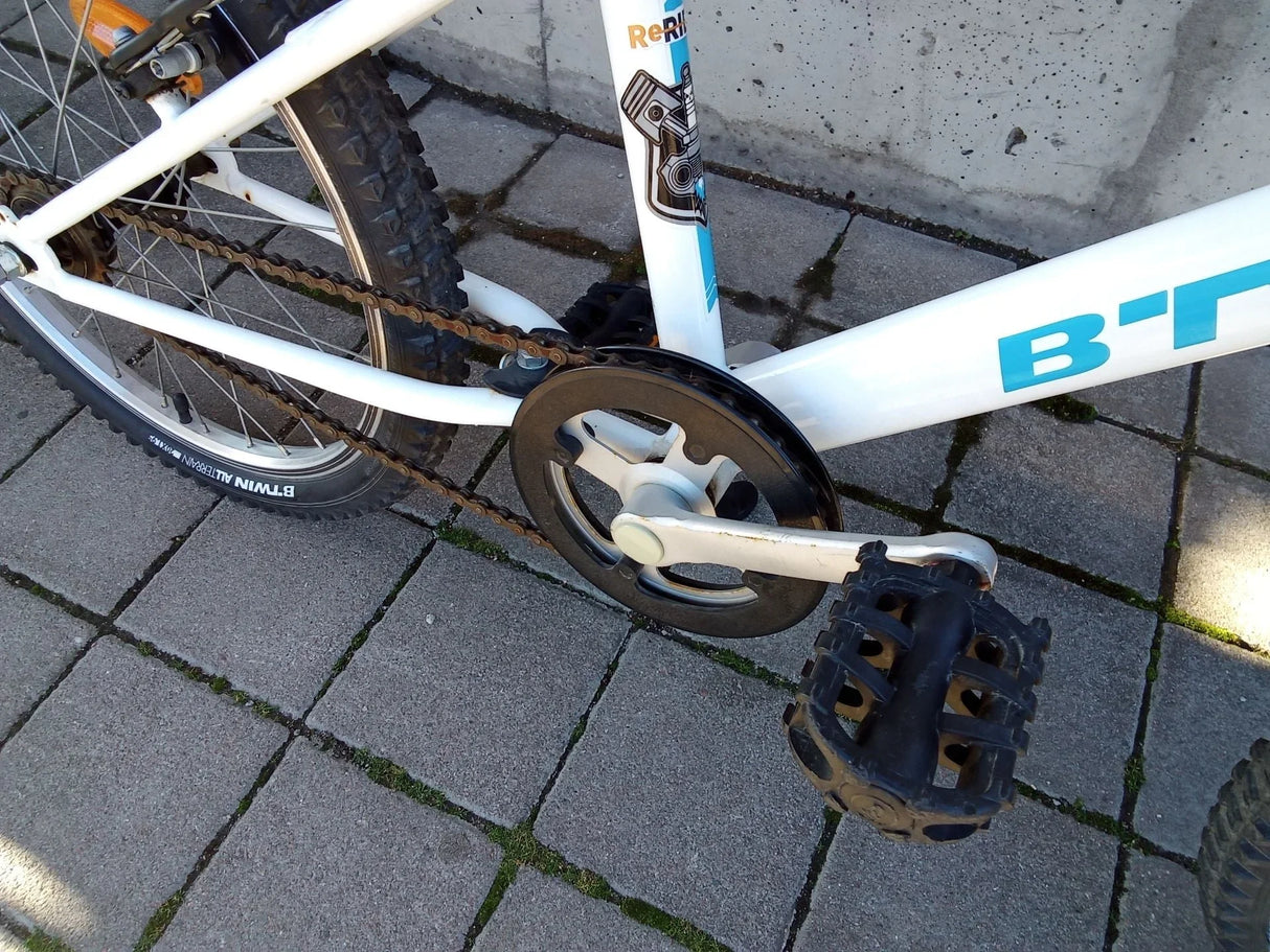 Vit BTWIN mountainbike med svart pedal och kedja på grått stenunderlag