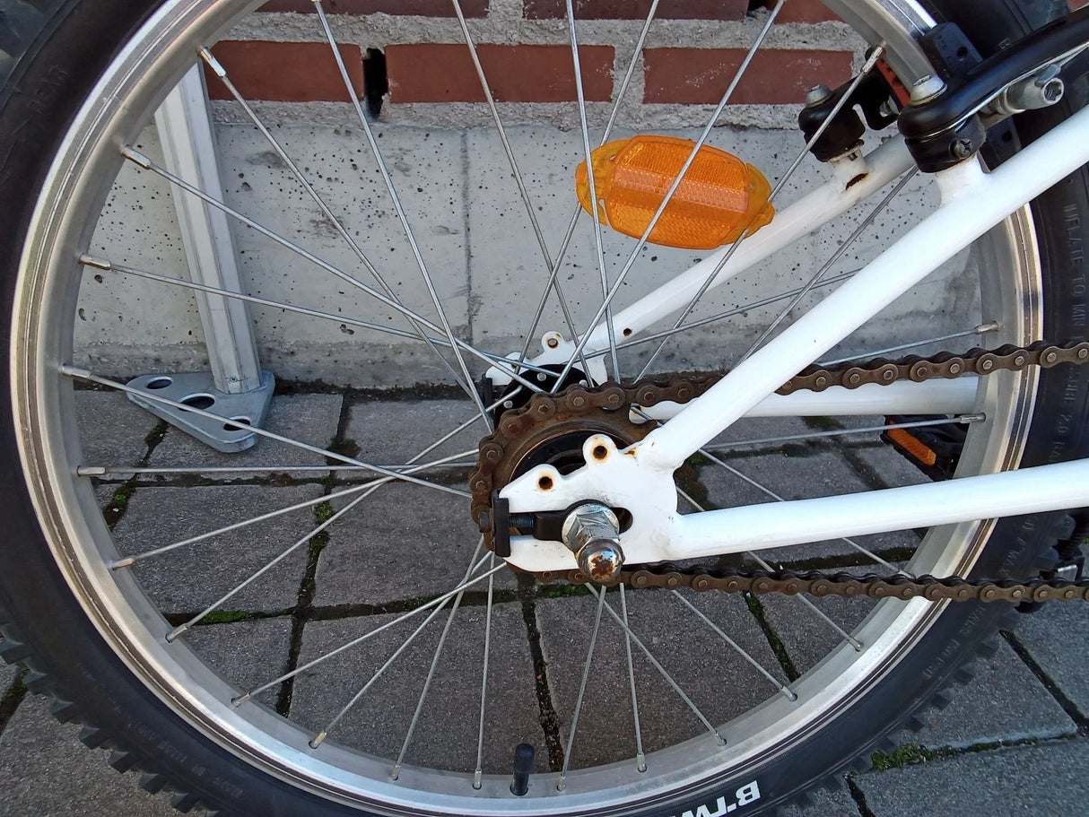 Bakhjul på vit cykel med cykelkedja, orange reflex och metall ekrar
