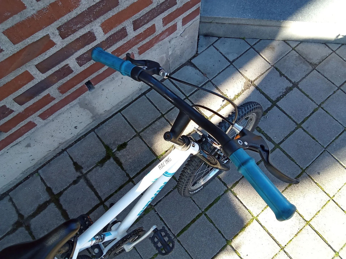 vit racing cykel med blå handtag och bromshandtag på trottoar med tegelvägg