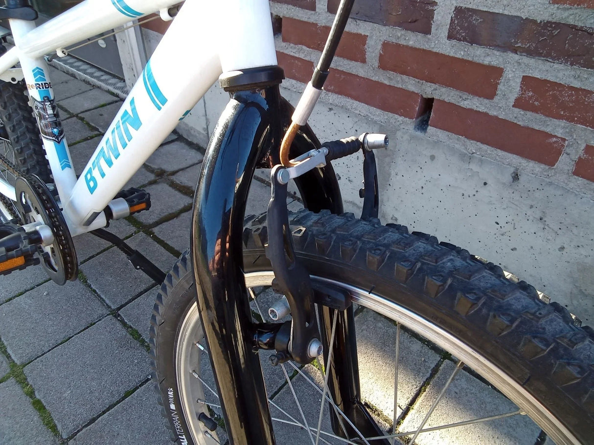 Närbild på framhjul och broms på vit och blå BTWIN barncykel med terrängdäck