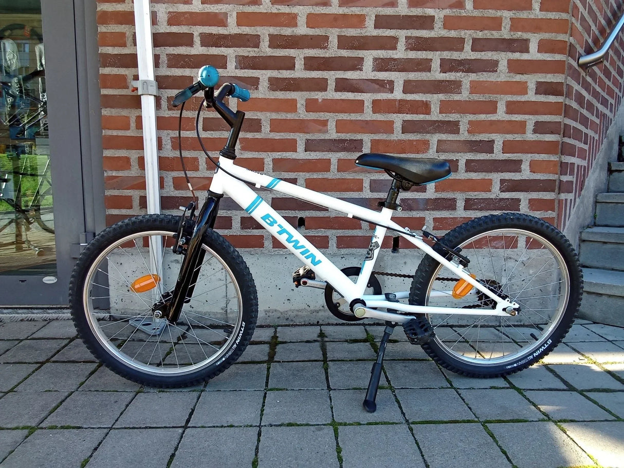 Vit och svart B-Twin barncykel med knäppa däck och blåa handtag