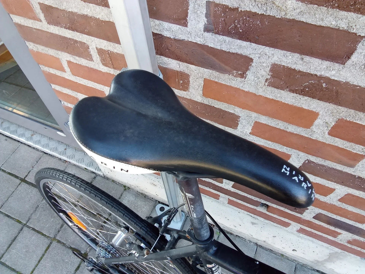 Svart cykelsadel med vit text monterad på en svart cykel nära tegelvägg