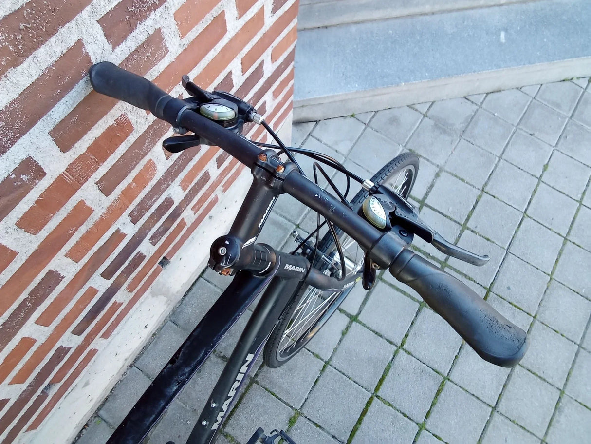 Svart cykel med styre, växelreglage och bromshandtag parkerad vid trottoar