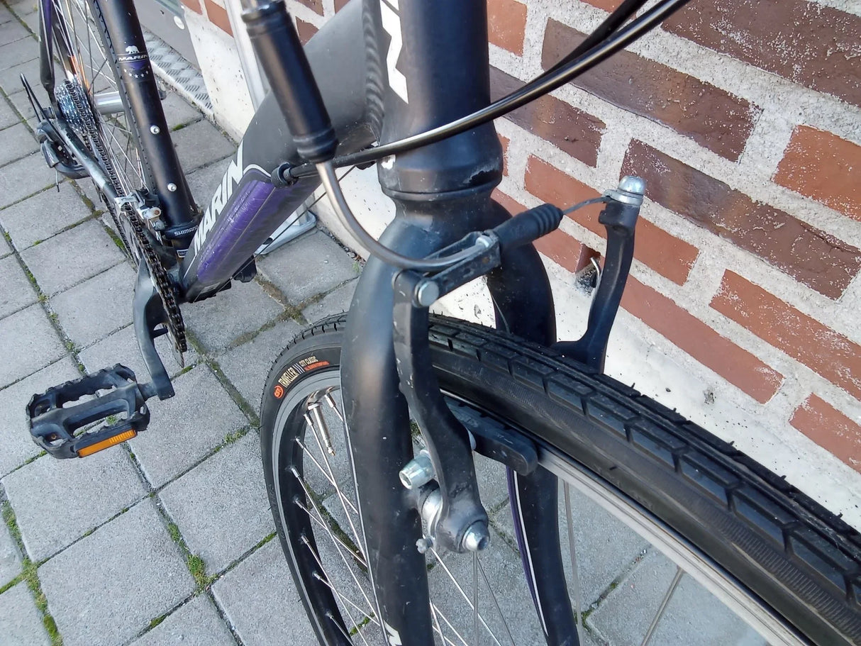 Närbild av framgaffel, bromssystem och framdäck på svart Marin cykel med Shimano komponenter