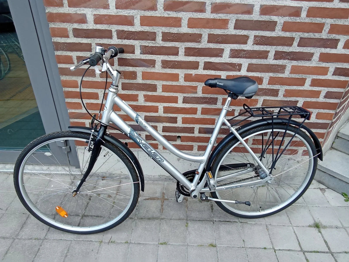 Silver cykel med svart sadel, svart pakethållare och däck på trottoar