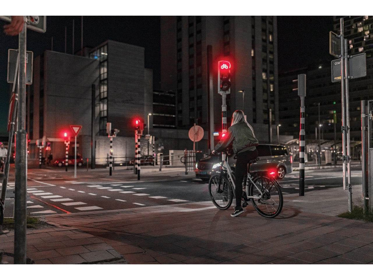 Cyklist väntar vid rött trafikljus på stadsgata med cykelöverfart på natten