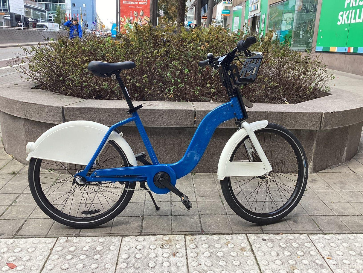 Blå och vit stadscykel parkerad på trottoar med svart cykelkorg på styret