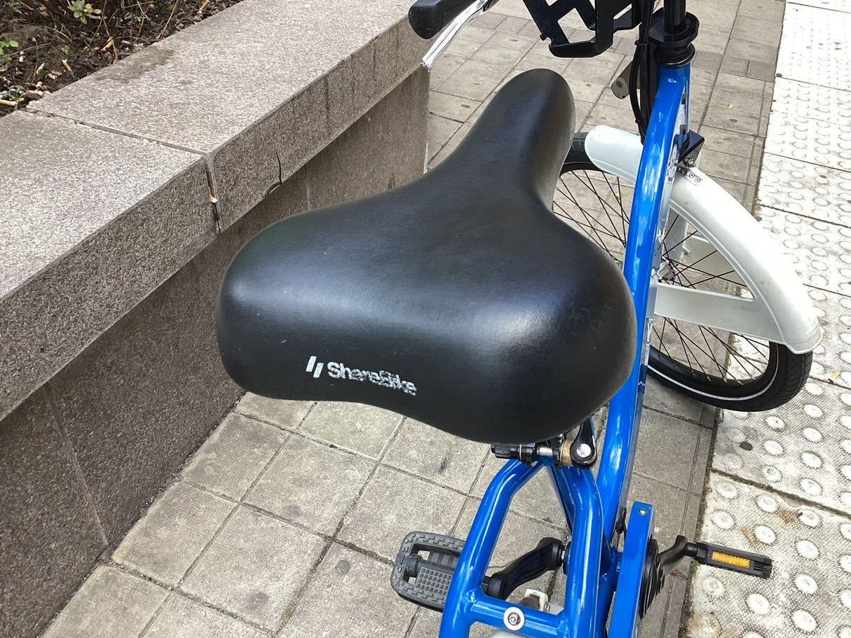 Svart cykelsadel på blå ram med vit skärm och trampor på stenplattor