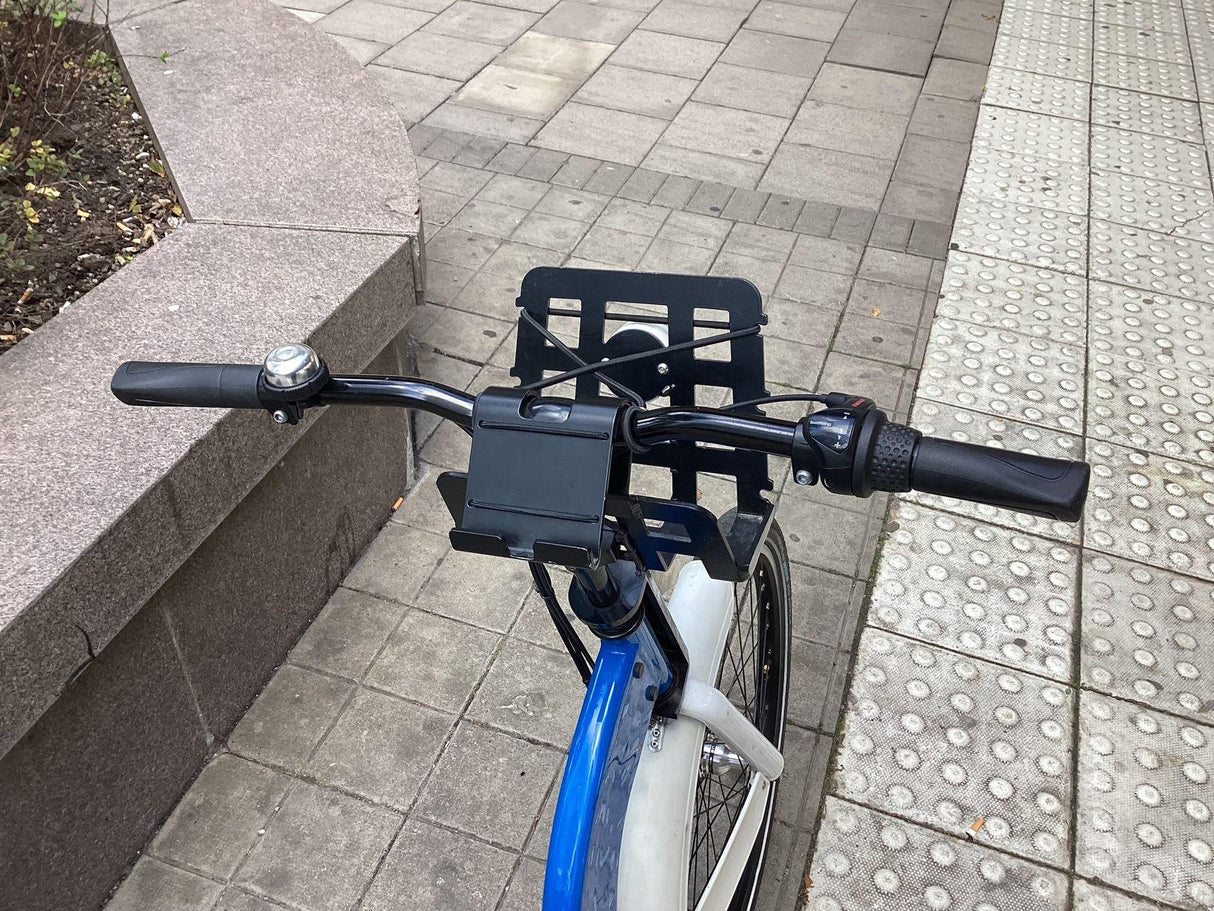 Närbild på cykelstyre med mobilhållare, handtag och ringklocka på trottoar
