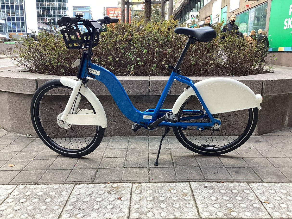 Blå och vit stadscykel med pakethållare och skärmar parkerad på trottoar